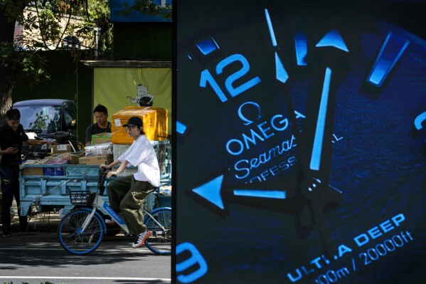 FILE - A woman rides past delivery workers who are sorting out parcels on a cart near a luxury watch advertising board at an outdoor shopping mall in Beijing on Sept. 20, 2023. China’s economy slowed in the third quarter, amid muted global demand, deflationary pressures and an ailing property sector. (AP Photo/Andy Wong, File)