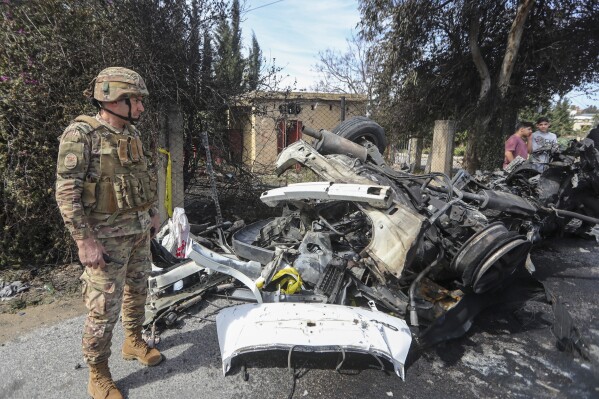 A Lebanese army officer stands next to a destroyed car in the southern outskirts of Tyre, Lebanon, Wednesday, March 13, 2024. An Israeli drone strike Wednesday targeting a car in southern Lebanon near the coastal city of Tyre killed a member of Hamas and at least one other person. (AP Photo/Mohammad Zaatari)