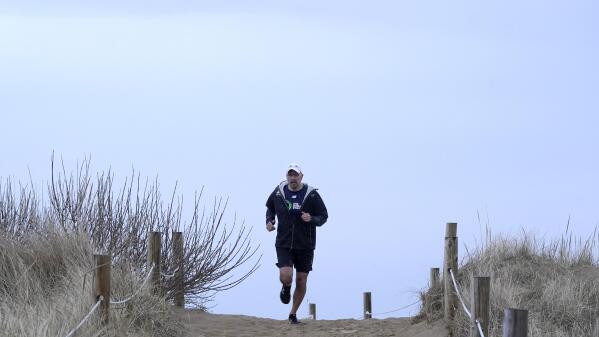 Dave Fortier, of Newburyport, Mass., president of One World Strong Foundation, trains for the 2023 Boston Marathon as he runs along a path to a beach Tuesday, April 4, 2023, in Newburyport. Fortier was hit in the foot by shrapnel in the 2013 bombing and doesn't remember finishing the race. (AP Photo/Steven Senne)