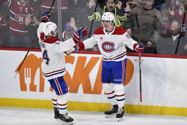 Montreal Canadiens' Justin Barron (52) celebrates after his winning goal against the Winnipeg Jets in overtime with Nick Suzuki (14) during NHL hockey game action in Winnipeg, Manitoba, Monday, Dec. 18, 2023. (Fred Greenslade/The Canadian Press via AP)
