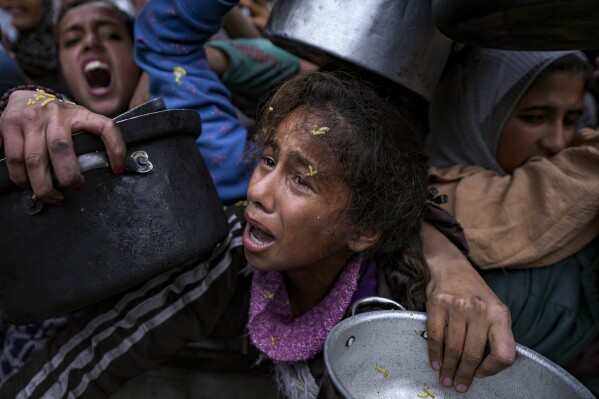 A Palestinian girl struggles to reach for food at a distribution center in Khan Younis, Gaza Strip, Friday, Dec. 20, 2024. (AP Photo/Abdel Kareem Hana)