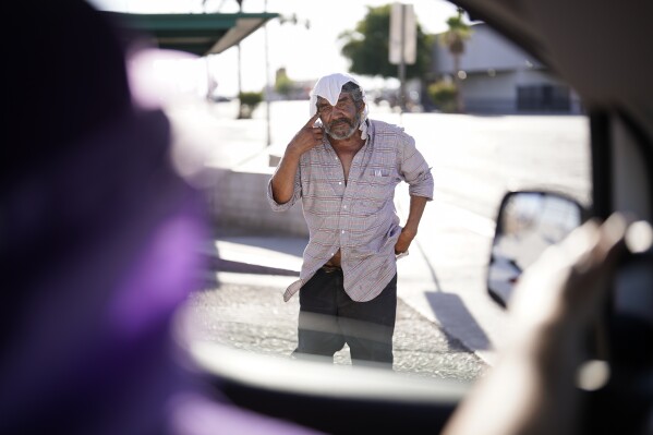 A man, who is homeless, talks to Maribel Padilla, left, of the Brown Bag Coalition, after receiving a cold, wet towel, Thursday, July 20, 2023, in Calexico, Calif. Once temperatures hit 113 degrees Fahrenheit (45 Celsius), Padilla and the Brown Bag Coalition meet up with people who are homeless in Calexico, providing them with cold, wet towels, and some refreshments to help them endure the scorching temperatures. (AP Photo/Gregory Bull)