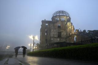 In this July 15, 2021, file photo, men walk in a heavy rain near the Atomic Bomb Dome in Hiroshima, western Japan. Japanese Prime Minister Yoshihide Suga said Monday, July 26, 2021, that he has decided to recognize 84 Hiroshima residents who were exposed to highly radioactive “black rain” just after the  U.S. atomic bombing as “hibakusha" eligible for official medical support. (AP Photo/Eugene Hoshiko, File)