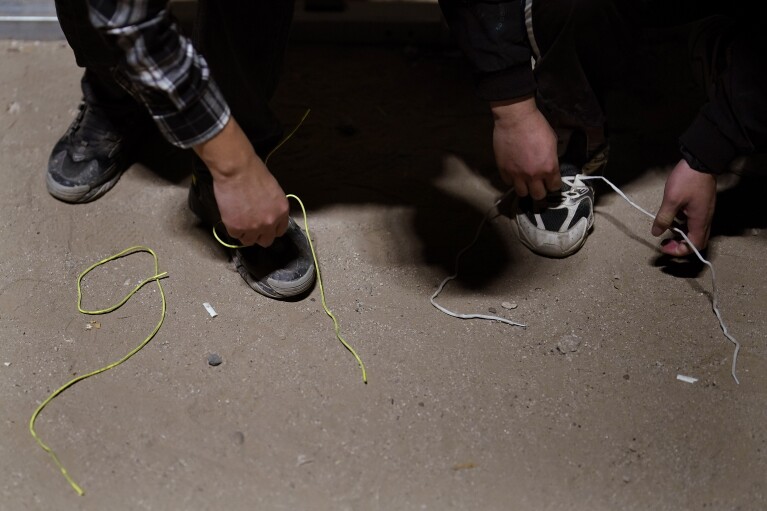 Two men remove their shoelaces as they wait to apply for asylum after crossing the border from Mexico Tuesday, July 11, 2023, near Yuma, Arizona. (AP Photo/Gregory Bull)