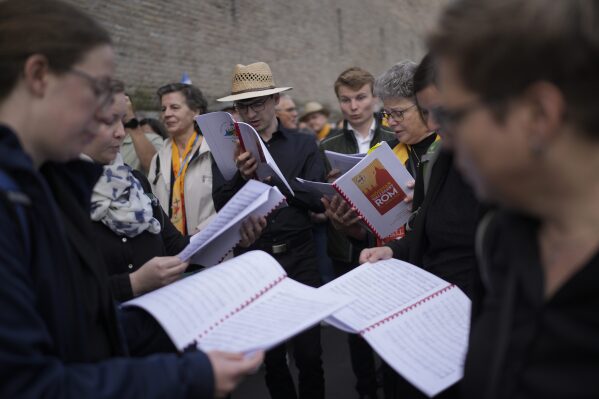 People look at booklets as they wait in line to view Pope Francis lying in state inside St. Peter's Basilica, at the Vatican, Thursday, April 24, 2025. (AP Photo/Markus Schreiber)