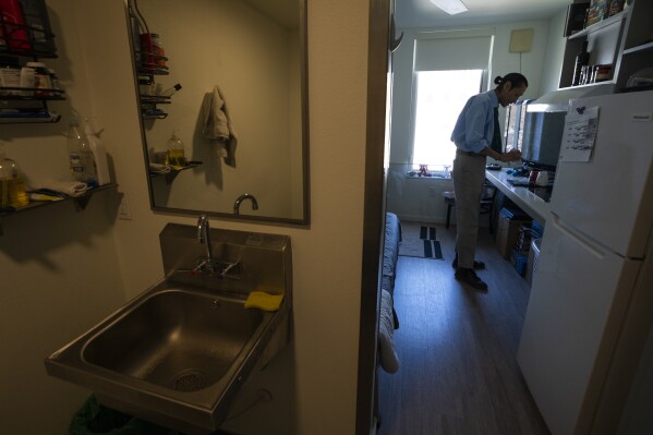 Cheyenne Welbourne is seen standing at his micro-apartment's kitchenette in the Starlight affordable housing building that is run by Central City Concern, a Portland-based homeless services nonprofit, on Friday, March 15, 2024, in Portland, Ore. Welbourne moved into one of the nonprofit's single room occupancy units in downtown Portland last March after years of living on the streets. (AP Photo/Jenny Kane)