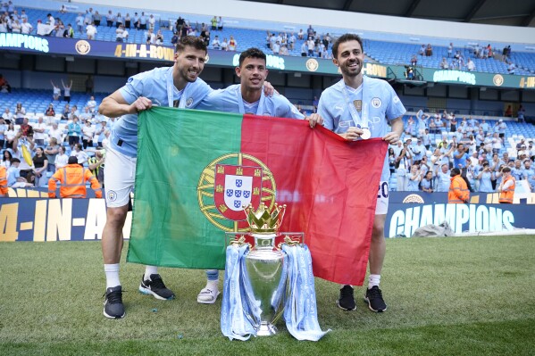 Manchester City's players Ruben Dias, left, Matheus Nunes, center, and Bernardo Silva celebrate with the Premier League trophy after the English Premier League soccer match between Manchester City and West Ham United at the Etihad Stadium in Manchester, England, Sunday, May 19, 2024. Manchester City clinched the English Premier League on Sunday after beating West Ham in their last match of the season. (AP Photo/Dave Thompson)