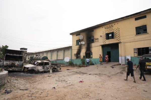 People walk past burned vehicles in front of a correctional facility in Owerri, Nigeria, on Monday, April 5, 2021. Hundreds of inmates escaped from the prison in southeastern Nigeria after a series of coordinated attacks according to government officials. (AP Photo/David Dosunmu)