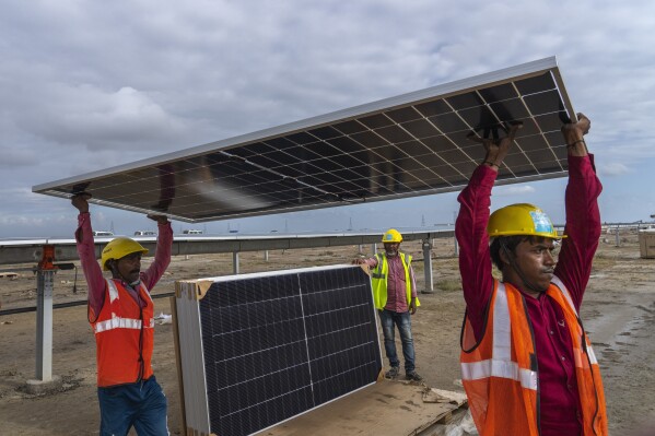 Workers carry a solar panel for installation at the under-construction Adani Green Energy Limited's Renewable Energy Park in the salt desert of Karim Shahi village, near Khavda, Bhuj district near the India-Pakistan border in the western state of Gujarat, India, Thursday, Sept. 21, 2023. India is developing a 30 gigawatt hybrid — wind and solar — renewable energy project on one of the largest salt deserts in the world. (AP Photo/Rafiq Maqbool)