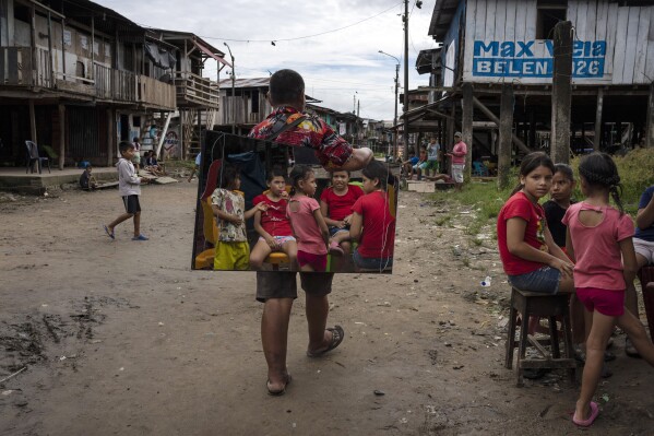 Children are reflected in a mirror of vendor Manolo Apagueno as he walks past in the Belen neighborhood of Iquitos, Peru, Saturday May 25, 2024. The Indigenous community in the heart of Peru's Amazon known as the "Venice of the Jungle" is hosting the Muyuna Floating Film Festival, celebrating tropical forests. (AP Photo/Rodrigo Abd)