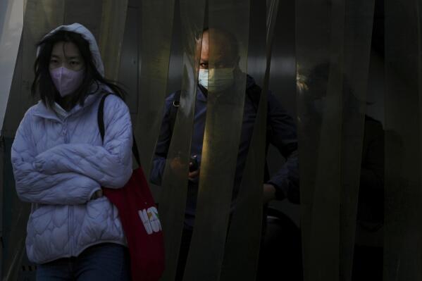 Commuters wearing face masks walk through the plastic curtain as they exit a subway station in Beijing, Monday, Oct. 31, 2022. (AP Photo/Andy Wong)