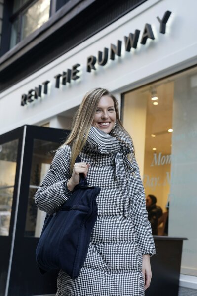 In this Monday, Nov. 25, 2019 photo, Vara Pikor poses for a picture in front of a "Rent The Runway" store before returning some items in New York. Pikor is wearing some of the items she rents from the company, including her jacket and earrings. Now a booming $1 billion business, the clothing rental sector is expected to reach $2.5 billion by 2023, says research firm GlobalData. But for traditional retailers, the economics of renting affordable clothing pose significant challenges.  (AP Photo/Seth Wenig)