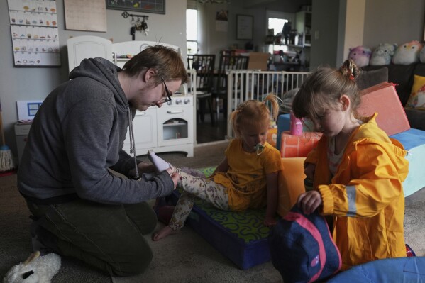 Kirt Ethridge, left, puts socks on his daughter, Naomi, 2, center, as his other daughter, Eliza, 5, gets a hat before a walk Thursday, April 10, 2025, in Evansville, Ind. (AP Photo/Joshua A. Bickel)