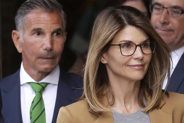 CORRECTS THAT GIANNULLI IS UNDER HOME CONFINEMENT - FILE - In this April 3, 2019, file photo, actress Lori Loughlin, front, and her husband, clothing designer Mossimo Giannulli, left, depart federal court in Boston after facing charges in a nationwide college admissions bribery scandal.    Giannulli has been released from a California prison, Saturday, April 3, 2021,  and is under home confinement following his imprisonment for his role in a college admissions bribery scheme.  (AP Photo/Steven Senne, File)
