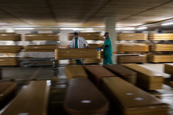 Workers move a coffin with the body of a victim of coronavirus as others coffins are stored waiting for burial or cremation at the Collserola morgue in Barcelona, Spain, Thursday, April 2, 2020. The new coronavirus causes mild or moderate symptoms for most people, but for some, especially older adults and people with existing health problems, it can cause more severe illness or death. (AP Photo/Emilio Morenatti)