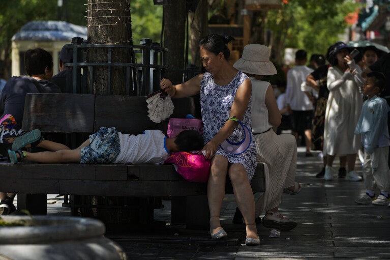 A woman uses a fan to cool a child as they sit on a bench at Qianmen pedestrian shopping street on a hot day in Beijing, Thursday, June 29, 2023. The entire planet sweltered for the two unofficial hottest days in human recordkeeping Monday and Tuesday, according to University of Maine scientists at the Climate Reanalyzer project. The unofficial heat records come after months of unusually hot conditions due to climate change and a strong El Nino event. (AP Photo/Andy Wong)