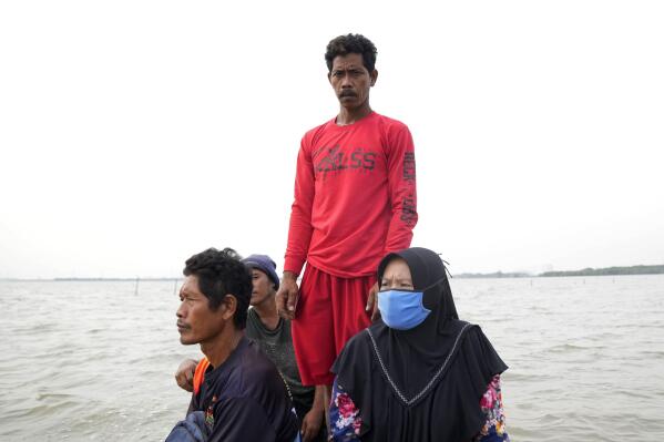 Aslori, en el centro, está de pie en un barco que lo lleva a él y a su esposa Asiyah, a la derecha, a su antigua casa en Modoliko, Java Central, Indonesia, el lunes 5 de septiembre de 2022. Los científicos dicen que partes de la isla se perderán por completo en el mar. en los próximos años. (Foto AP/Dita Alangkara)