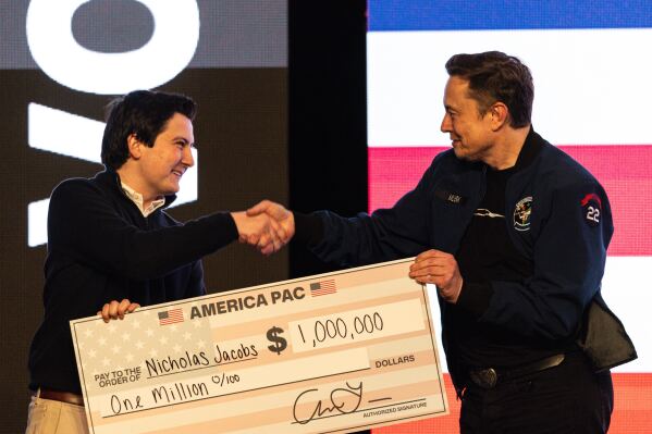 Elon Musk hands over a million dollar check to Nicholas Jacobs during a town hall in Green Bay, Wis., March 30, 2025. (AP Photo/Jeffrey Phelps, File)