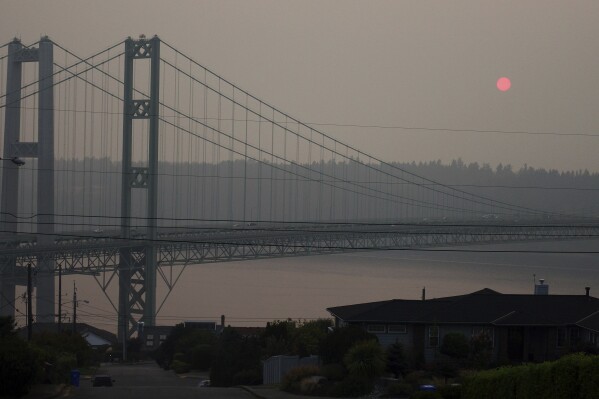 FILE - The sun sets through smoky air behind the Narrows Bridge in Tacoma, Wash., on Aug. 19, 2018. A coroner's investigation into the death of a man in Los Angeles in February 2024 revealed that he was a suspect in a 2008 Washington state child rape who was believed to have jumped to his death from a bridge on Puget Sound years ago, authorities said. A witness reported seeing the man jump from the Tacoma Narrows Bridge on March 29, 2009. (AP Photo/Ted S. Warren, File)