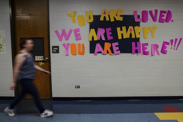 A staff member walks past a message to students that hangs on the wall at Place Bridge Academy, May 20, 2025, in Denver. (AP Photo/Rebecca Slezak)