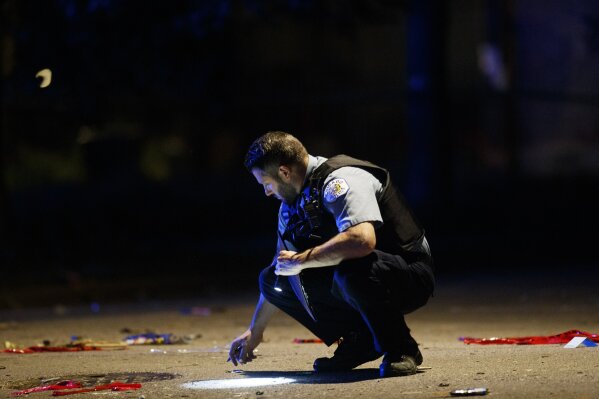 FILE - In this July 5, 2020, file photo, an officer investigates the scene of a shooting in Chicago. Still reeling from the coronavirus pandemic and street protests over the police killing of Floyd, exhausted cities around the nation are facing yet another challenge: A surge in recent shootings has left dozens dead, including young children. (Armando L. Sanchez/Chicago Tribune via AP, File)