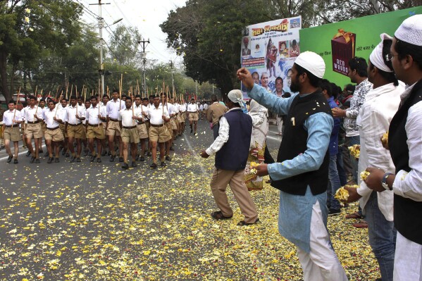 FILE – In this Feb. 23, 2014 file photo, Indian Muslims shower flower petals as volunteers of Hindu nationalist group Rashtriya Swayamsevak Sangh, (RSS), march on the concluding day of their three-day meeting in Bhopal, India. For the RSS, Indian civilization is inseparable from Hinduism. (AP Photo/Rajeev Gupta, File)