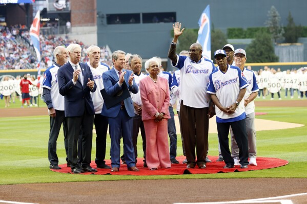 Billye Aaron, center, wife of the late Hank Aaron, stands with Georgia Gov. Brian Kemp, second from front left, Atlanta Braves chairman and CEO Terry McGuirk, front left, Dusty Baker, fourth from right, and players from the 1974 Braves team during a ceremony to mark the 50th anniversary of Hank breaking Babe Ruth's home run record team, before a baseball game against the New York Mets, Monday, April 8, 2024, in Atlanta. (Miguel Martinez/Atlanta Journal-Constitution via AP)