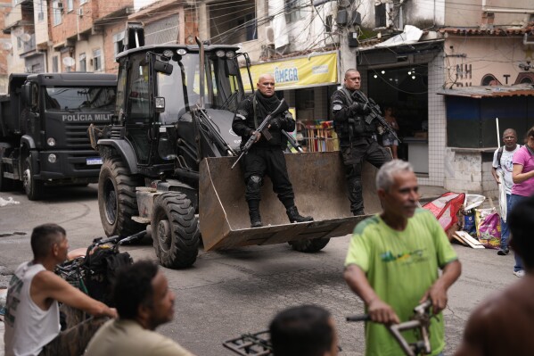 FILE - Police ride past residents in a bulldozer they use to clear street barricades during a security operation against organized crime in the Mare Complex favela of Rio de Janeiro, Brazil, Oct. 9, 2023. The Brazilian Supreme Court ruled on Thursday, April 12, 2024, that the state must compensate victims of stray bullets during military and law enforcement operations. (AP Photo/Silvia Izquierdo, File)