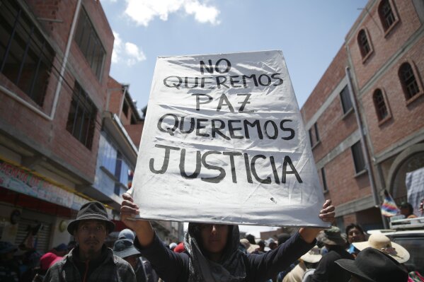 A supporter of former President Evo Morales holds a sign with a handwritten message that reads in Spanish: "We don't want peace, We want justice," during a protest at a blocked highway in El Alto, on the outskirts of La Paz, Bolivia, Wednesday, Nov. 20, 2019. Bolivia has been in a state of turbulence since a disputed Oct. 20 vote. Morales resigned Nov. 10, but his supporters oppose the interim government that took his place. (AP Photo/Natacha Pisarenko)