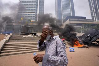 Un hombre se cubre el rostro por los gases lacrimógenos mientras camina frente a un campamento destrozado de manifestantes antigubernamentales frente a la oficina del presidente en Colombo, Sri Lanka, el lunes 9 de mayo de 2022. (Foto AP/Eranga Jayawardena)