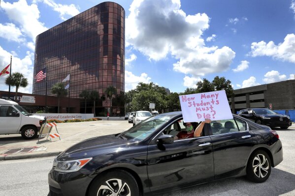 FILE - In this July 7, 2020, file photo, a teacher holds up a sign while driving by the Orange County Public Schools headquarters as educators protest in a car parade around the administration center in downtown Orlando, Fla. As the Trump administration pushes full steam ahead to force schools to resume in-person education, public health experts warn that a one-size-fits-all reopening could drive infection and death rates even higher. (Joe Burbank/Orlando Sentinel via AP, File)