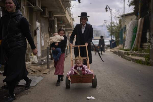 A child is transported on a dolly in the Orthodox neighborhood of Mea Shearim in Jerusalem during final preparations for the Passover holiday, April 11, 2025. (AP Photo/Ohad Zwigenberg)