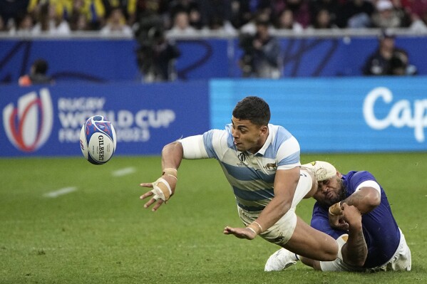 Argentina's Santiago Chocobares, left, passes the ball as he is tackled by Samoa's Alai D'Angelo Leuila during the Rugby World Cup Pool D match between Argentina and Samoa at the Stade Geoffroy Guichard in Saint-Etienne, France, Friday, Sept. 22, 2023. (AP Photo/Laurent Cipriani)