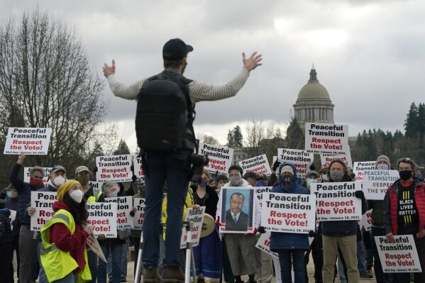 People hold signs as they assemble for a group photo following a vigil supporting a peaceful transition from President Donald Trump to President-elect Joe Biden, Monday, Jan. 18, 2021, in Olympia, Wash. More than 100 people took part in the demonstration ahead of Biden's upcoming inauguration on Wednesday. (AP Photo/Ted S. Warren)