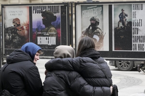 Young people sit near a street exhibition of military posters named 'Together to Victory' dedicated to Russian army in St. Petersburg, Russia, Monday, Feb. 24, 2025. (AP Photo/Dmitri Lovetsky)
