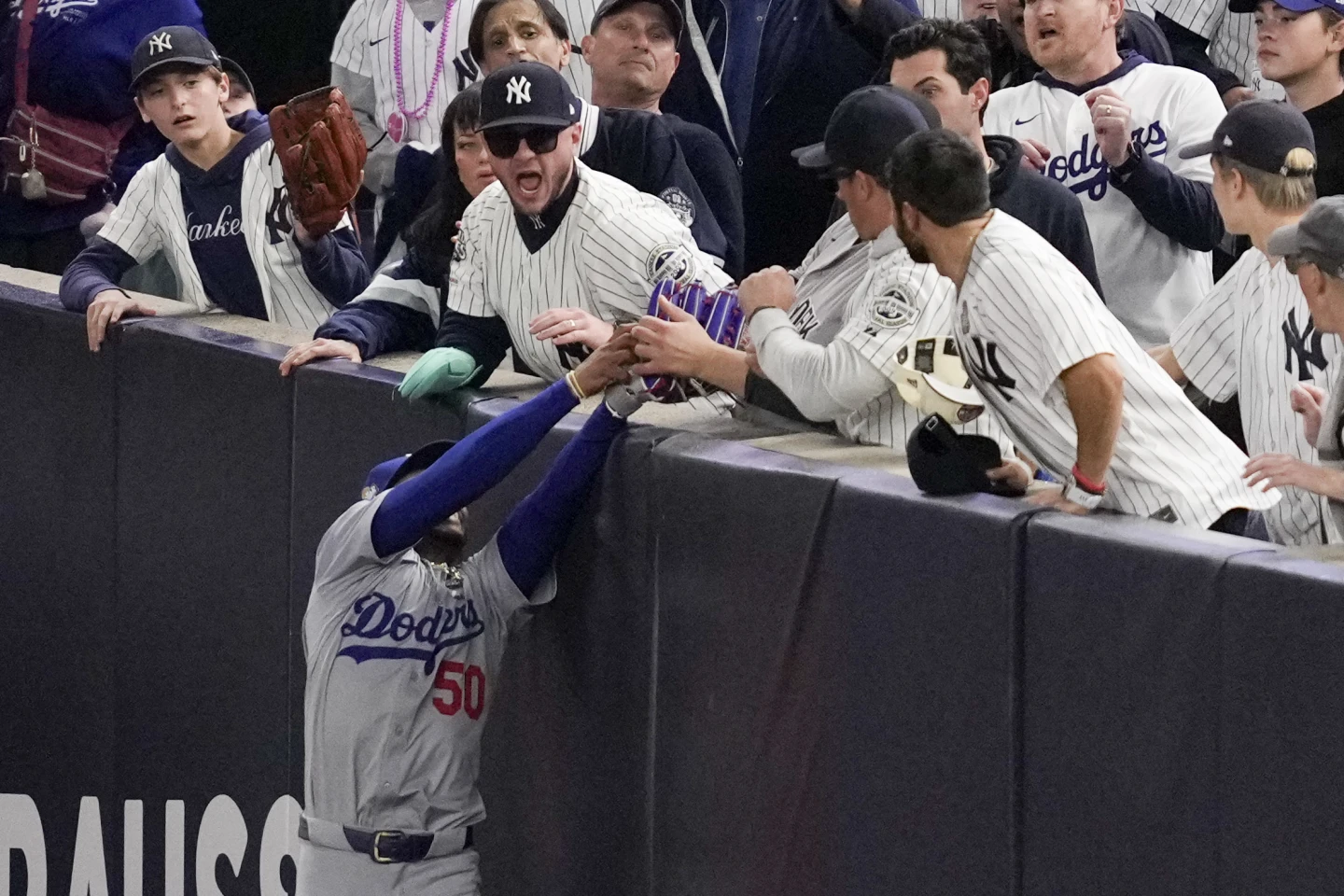 Fans interfere with a foul ball caught by LA Dodgers right fielder Mookie Betts during the first inning in Game 4 of the baseball World Series against the New York Yankees, Tuesday, Oct. 29, 2024, in New York.