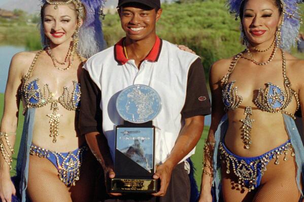 FILE - In this Oct. 6, 1996, file photo, Tiger Woods, center, poses with Ballys' Jubilee dancers Windi See, left, and Gracie Martinez after winning his first pro golf tournament at the Las Vegas Invitational in Las Vegas. Twenty-five years ago this week Woods won for the first time on the PGA Tour at the Las Vegas Invitational, changing golf forever. (AP Photo/Lennox McLendon, File)