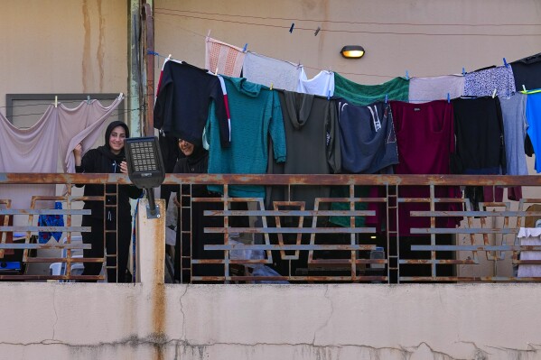 Residents displaced from their homes in southern Lebanon by clashes on the border with Israel stand on a balcony at a hotel being used as a shelter in the southern town of Marwanieh, Lebanon, Friday, March 15, 2024. (AP Photo/Bilal Hussein)