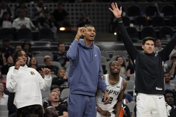 From left to right, San Antonio Spurs center Khem Birch, center Victor Wembanyama, guard Malaki Branham and forward Doug McDermott cheer from the bench during the second half of a preseason NBA basketball game against the Houston Rockets in San Antonio, Monday, Oct. 16, 2023. (AP Photo/Eric Gay)