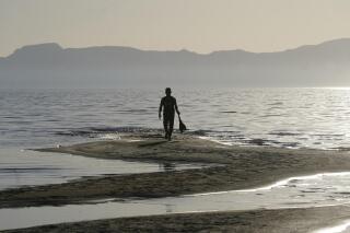 A man walks along a sand bar at the receding edge of the Great Salt Lake on June 13, 2021, near Salt Lake City. The lake has been shrinking for years, and a drought gripping the American West could make this year the worst yet. The receding water is already affecting nesting pelicans that are among millions of birds dependent on the largest natural lake west of the Mississippi River. (AP Photo/Rick Bowmer)