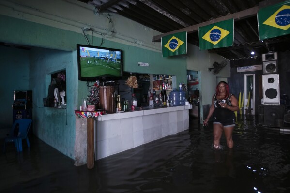 Heloisa Regina walks inside her flooded bar after deadly, heavy rainfall in Duque de Caxias, Brazil, Sunday, Jan. 14, 2024. (AP Photo/Bruna Prado)