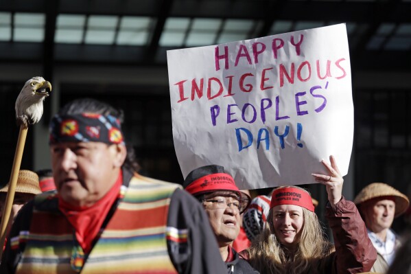 FILE - A sign is held aloft during an Indigenous Peoples Day march, Oct. 9, 2017, in Seattle. Native American people will celebrate their centuries-long history of resilience on Monday, Oct. 9, 2023, through ceremonies, dances and speeches. The events across the United States will come two years after President Joe Biden officially commemorated Indigenous Peoples Day. (AP Photo/Elaine Thompson, File)