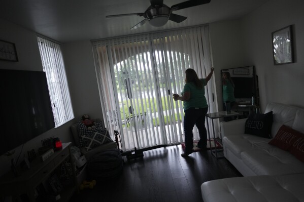 Melissa Lombana, 43, a high school teacher and mountain bike enthusiast, adjusts the blinds inside her one-bedroom apartment in Miramar, Fla., Wednesday, July 26, 2023. Lombana's rent has increased each of the last two years and now amounts to nearly half her monthly income. 