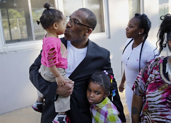 CORRECTS NOT GUILTY DATE TO 2016 - FILE - Anthony Wright gets a kiss from his granddaughter Romera Wright, 1, and holds on tight to his other granddaughter, Daria Wright, 8, while spending time with his family after walking out of Curran Fromhold Correctional Facility a free man on Aug. 23, 2016, in Philadelphia. In 2016 a jury found Wright not guilty in his retrial in the rape and murder of a 77-year-old woman a quarter-century ago, after DNA evidence pointed to another man. (Michael Bryant/The Philadelphia Inquirer via AP, File)