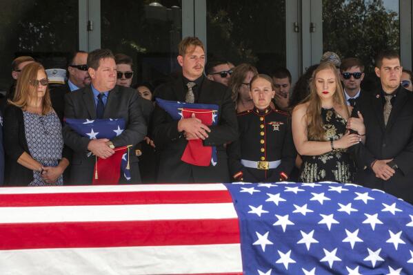 After the service for fallen Marine Sgt. Nicole Gee, her father Richard Herrera, left, and husband Jarod Gee hold U.S. flags at Bayside Church's Adventure Campus in Roseville, Calif., Saturday, Sept. 18, 2021, as her casket is moved to the hearse. Sgt. Gee lost her life, along with 12 other U.S. service members, in the bombing attack at the Kabul airport in Afghanistan on Aug. 26. (Renee C. Byer/The Sacramento Bee via AP)