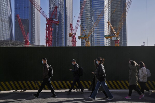 FILE - People wearing face masks walk by construction cranes near the office buildings at the central business district in Beijing, on March 15, 2023. Chinese leaders have held an annual planning meeting where they agreed to step up spending to help rev up the world's second-largest economy, state media reported Friday Dec. 8, 2023 without giving details of any policy changes. The report gave few specifics on how the leadership plans to handle fast mounting debts and resolve a crisis in the vital property sector after defaults by dozens of developers. (AP Photo/Andy Wong, File)
