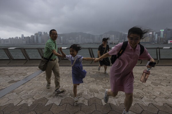 Mainland Chinese tourists run along a promenade during a typhoon in Hong Kong, Monday, July 17, 2023. Schools and the stock market were closed in Hong Kong on Monday as Typhoon Talim swept south of the city. (AP Photo/Louise Delmotte)