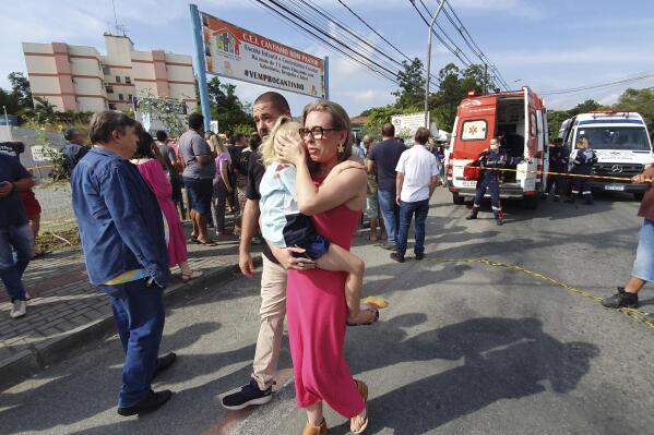 A woman conforts a crying girl outside the daycare center "Cantinho do Bom Pastor" after a fatal attack on children in Blumenau, Santa Catarina state, Brazil, Wednesday, April 5, 2023. A man with a hatchet jumped over a wall and invaded the daycare center, killing four children and wounding at least five others, authorities said. (Patrick Rodrigues/Portal NSC Total via AP)