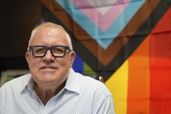 Robert Boo, CEO of the Pride Center at Equality Park, poses with a Progress Pride flag in his office at the community center supporting the local LGBTQ+ community and their allies, Wednesday, Jan. 17, 2024, in Wilton Manors, Fla. A bill Republican lawmakers are seeking in Florida would ban teachers from wearing a rainbow flag lapel pin for even a day, but allow them to hang a full-size North Korean or Iranian flag for as long as they want. A House committee approved the bill on a 9-5 vote Wednesday, Jan. 17, 2023. (AP Photo/Rebecca Blackwell)