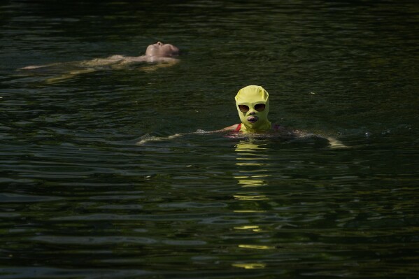 A woman wearing sun protection headgear and sunglasses swims as residents cool off on a sweltering day at an urban waterway in Beijing, Monday, July 10, 2023. (AP Photo/Andy Wong)